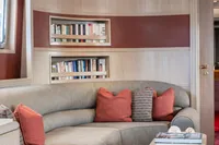 Luxurious yacht interior with curved sofa, red accents, and built-in bookshelves.