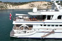 38m Nicolini motor yacht, 1986, cruising near scenic cliffs with a small boat on deck.