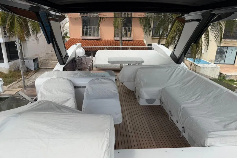 Atkun Yacht Photos Pics 2021 Sunseeker Manhattan 68 yacht deck with covered seating and table, surrounded by palm trees.