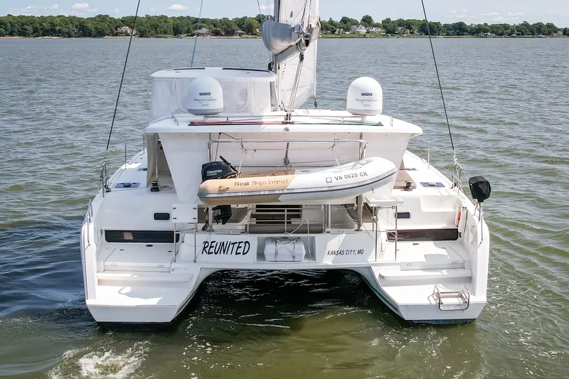 Reunited Yacht Photos Pics 2017 Lagoon 42 catamaran on water, rear view with dinghy and "Reunited" name.