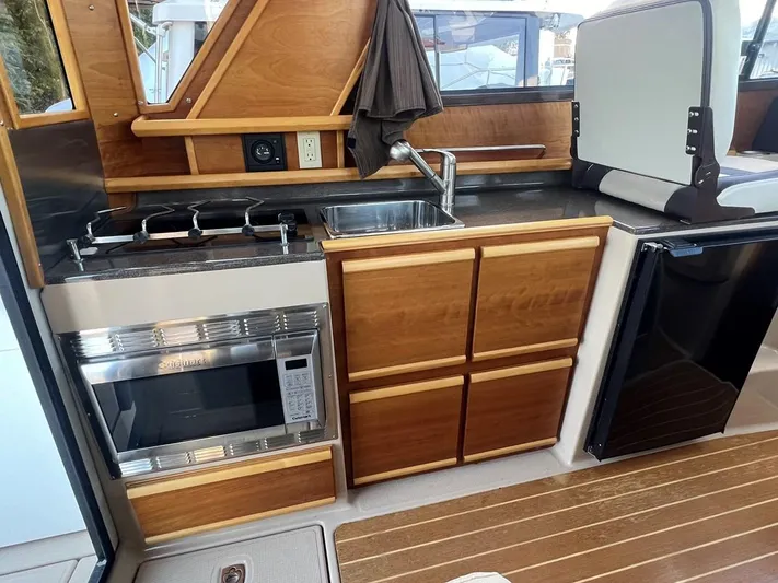  Yacht Photos Pics 2016 Cutwater C-28 boat kitchen with stove, sink, microwave, and wooden cabinetry.