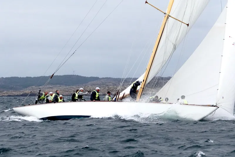 Wings K-15 Yacht Photos Pics Classic 1937 12-metre sailboat navigating choppy waters with crew, rocky coastline in background.