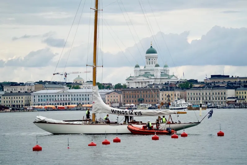 Wings K-15 Yacht Photos Pics Classic 1937 12-metre sailboat on water with cityscape and cathedral in background.