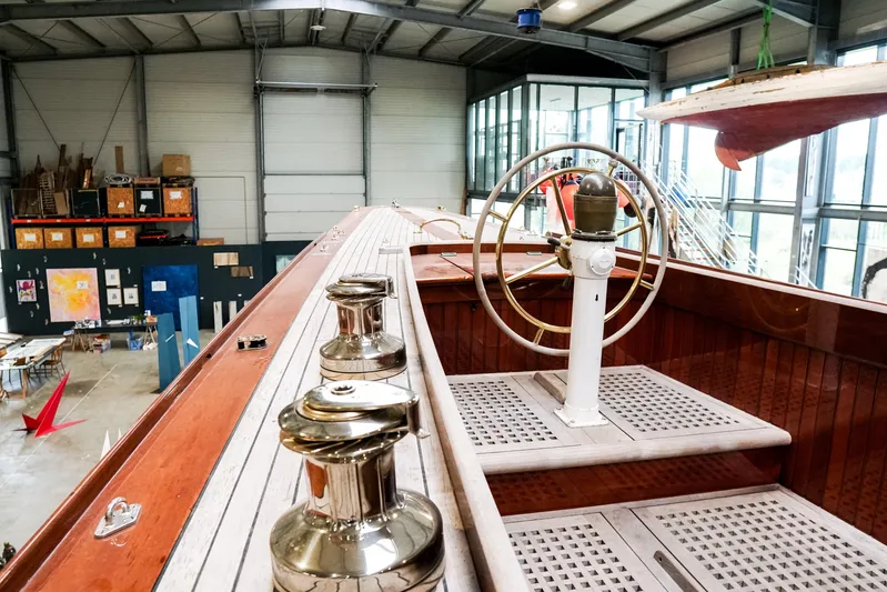 Wings K-15 Yacht Photos Pics 1937 Classic 12-metre yacht interior with wooden deck and vintage steering wheel in a workshop.