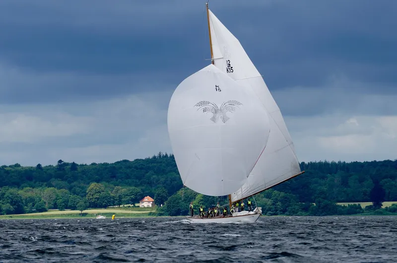 Wings K-15 Yacht Photos Pics Classic 1937 12-metre sailboat with large white sail on a lake under cloudy skies.