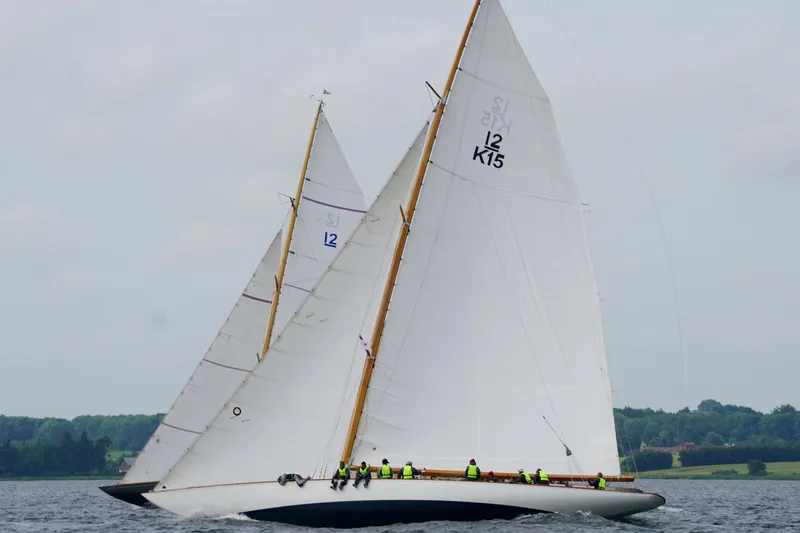 Wings K-15 Yacht Photos Pics Classic 1937 12-metre sailboats racing on a calm lake with lush green shoreline.