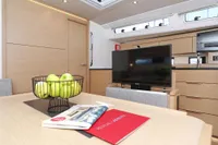 Modern interior of 2022 Hanse 460 yacht with TV, apples, and brochures on table.