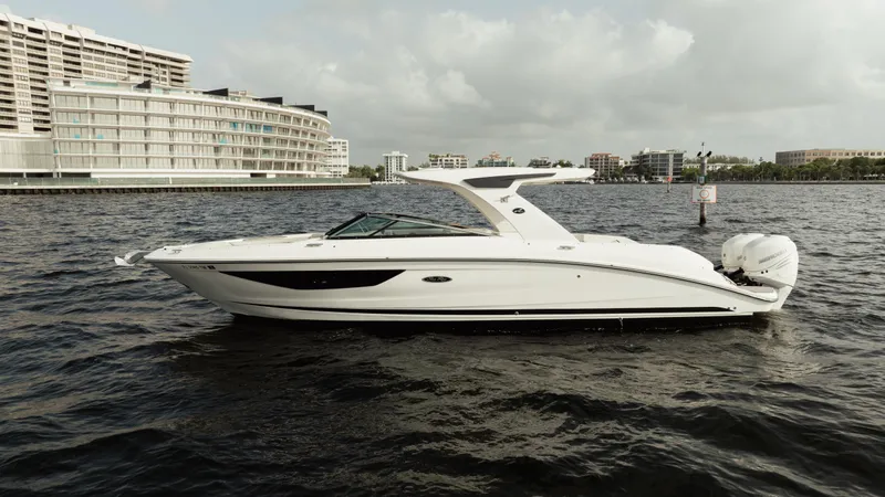  Yacht Photos Pics 2023 Sea Ray 350 Sundancer yacht on water, with modern buildings in the background.