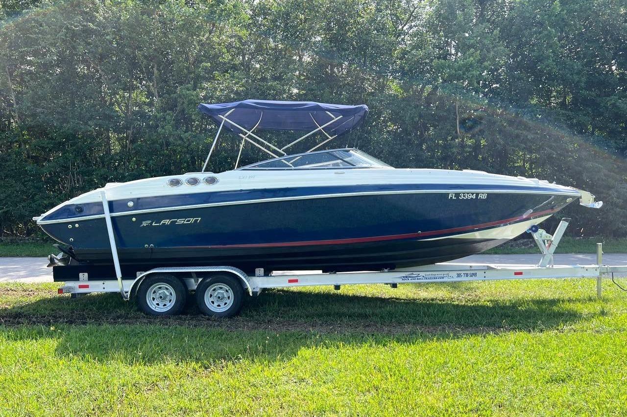 2013 Larson LXi 292 IO boat on trailer, parked on grass with trees in background.