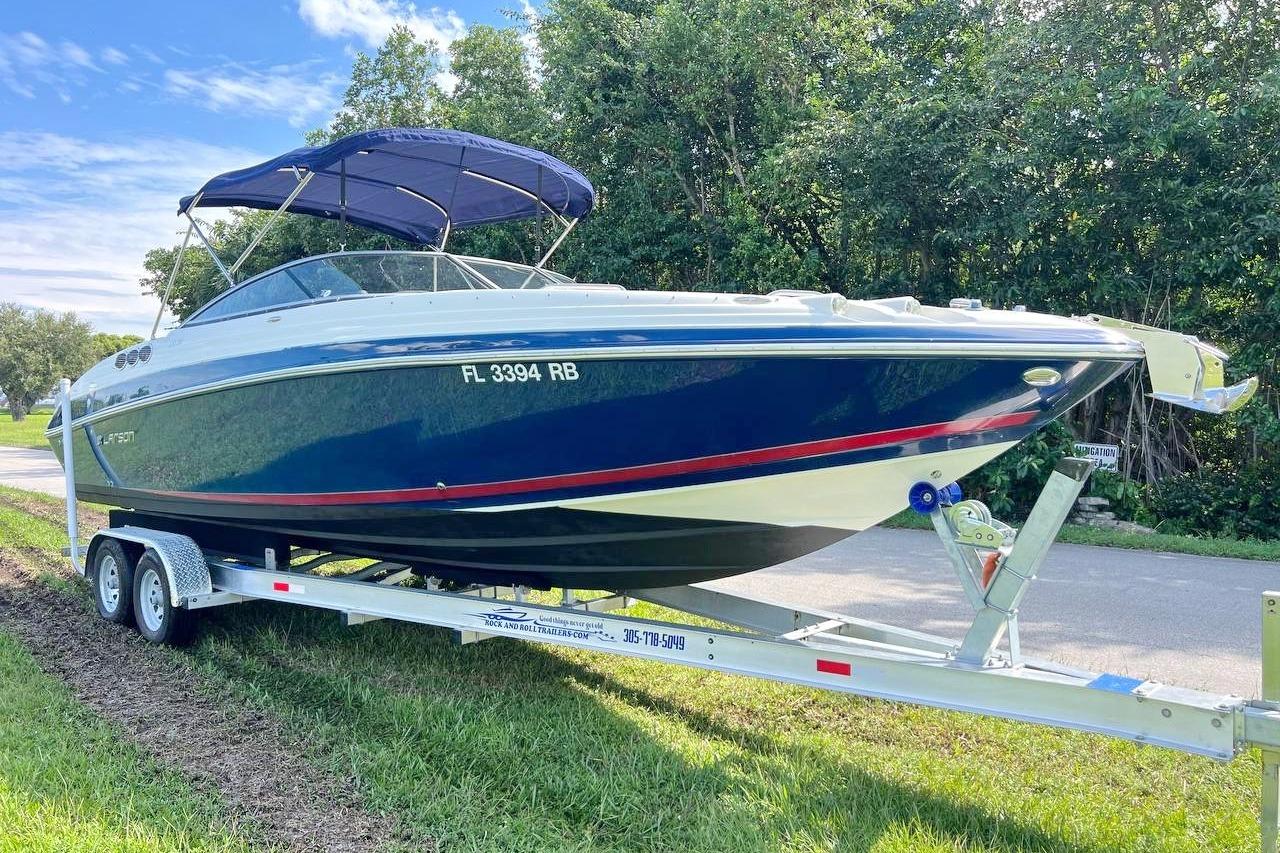 2013 Larson LXi 292 IO boat on trailer, parked near trees and road.
