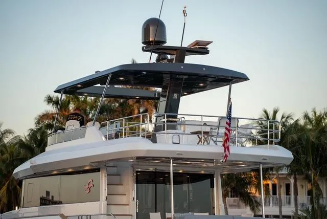 Freedom Yacht Photos Pics 2022 Sirena 58 Flybridge yacht with sleek design and American flag, docked near palm trees.