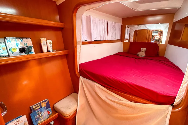 Sailifi Yacht Photos Pics Cozy cabin interior of 2007 Lagoon 440 catamaran with red bedding and books on shelves.
