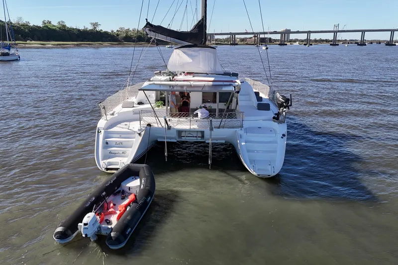 Sailifi Yacht Photos Pics 2007 Lagoon 440 catamaran with dinghy, anchored on calm waters near a bridge.