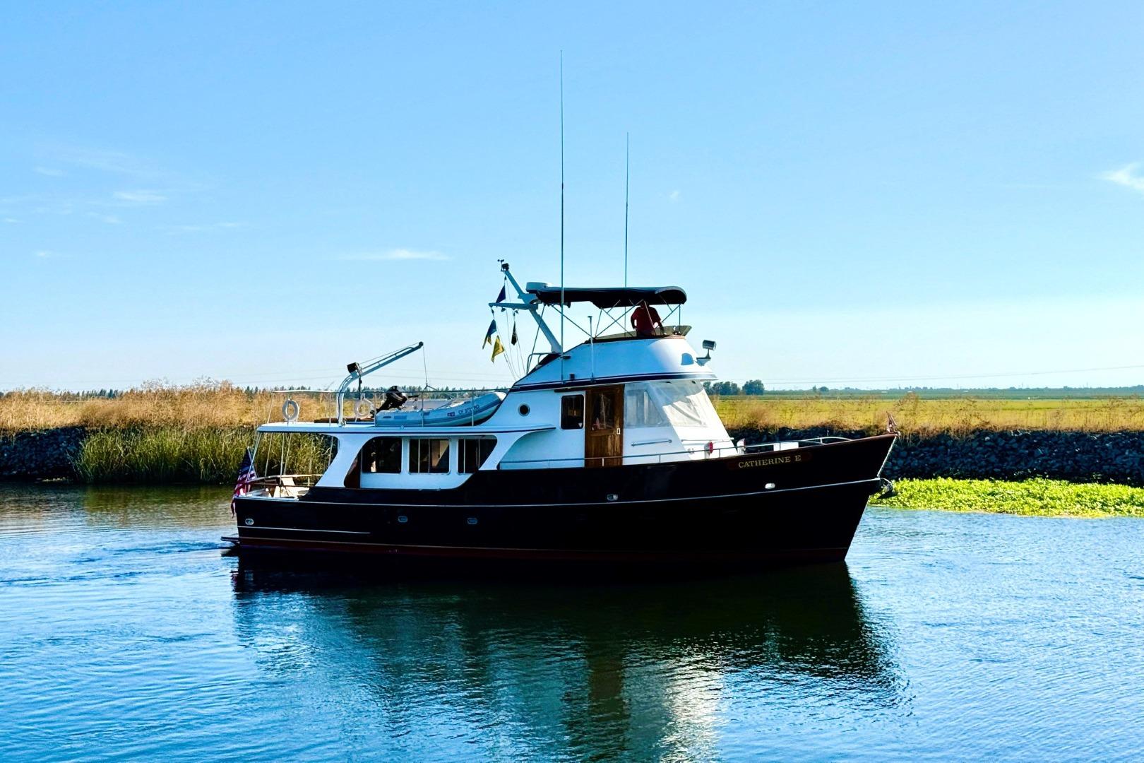 Custom 1989 52 Pilothouse boat cruising on a calm river under a clear blue sky.