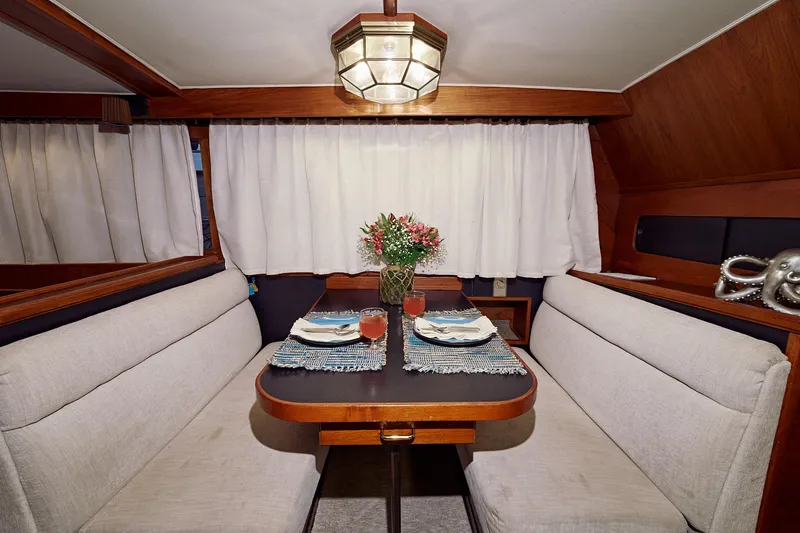 Camelot Yacht Photos Pics 1976 Pacemaker 65 yacht interior dining area with table, flowers, and cushioned seating.