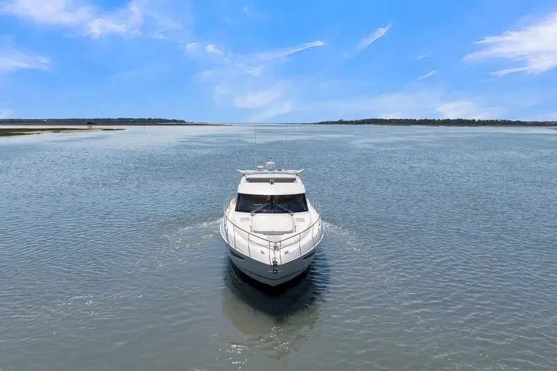 Yacht Photos Pics 2020 Riviera 4800 Sport Yacht cruising on a serene, open waterway under a clear blue sky.