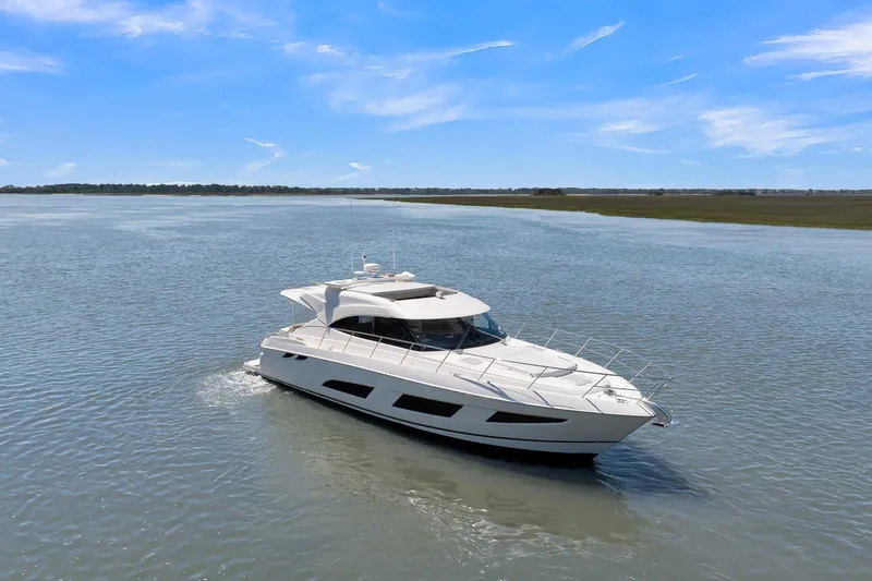  Yacht Photos Pics 2020 Riviera 4800 Sport Yacht cruising on a calm, scenic waterway under a clear blue sky.