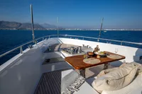 Luxurious deck of 2012 Bering 60 yacht with dining setup, overlooking serene ocean and distant coastline.
