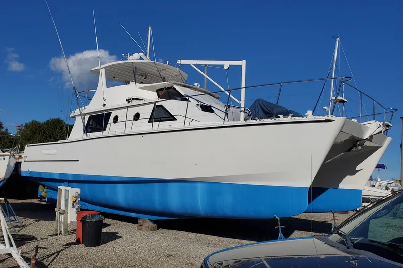 Nantucket Sleighride Yacht Photos Pics Custom 2005 Sea Raider Catamaran with blue hull, docked on gravel under clear sky.