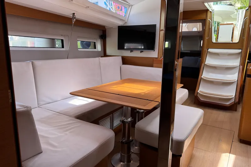 Reventador Yacht Photos Pics Interior of 2018 Jeanneau Sun Odyssey 440 yacht with white seating and wooden table.