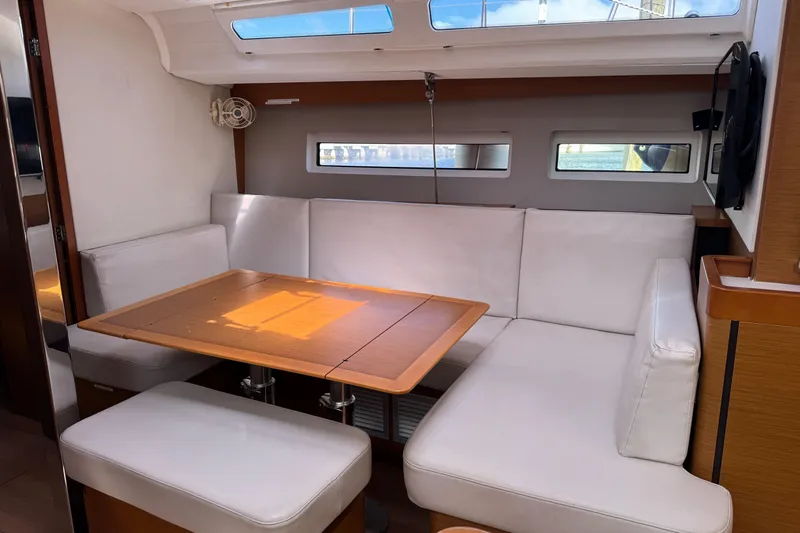 Reventador Yacht Photos Pics Interior of 2018 Jeanneau Sun Odyssey 440 yacht with white seating and wooden table.