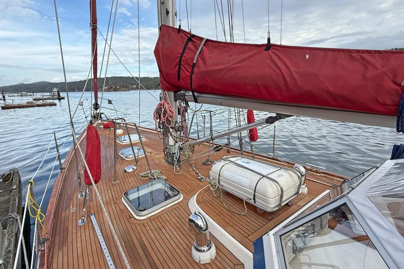 Raison D'etre Yacht Photos Pics 1988 Hallberg Rassy 42E sailboat deck with red sail cover and lifeboat, docked by calm waters.