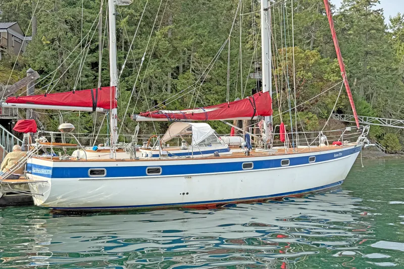 Raison D'etre Yacht Photos Pics 1988 Hallberg Rassy 42E sailboat with red sails docked in a serene forest setting.