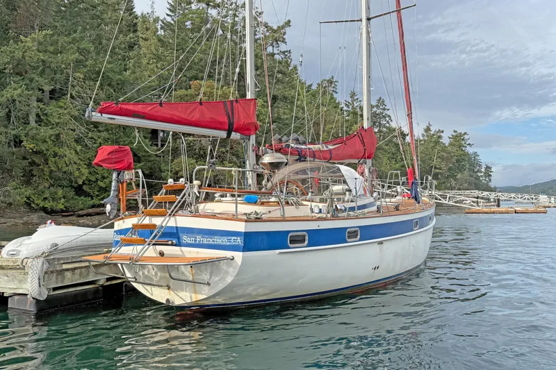 Raison D'etre Yacht Photos Pics 1988 Hallberg Rassy 42E sailboat docked, featuring red sails and lush forest backdrop.