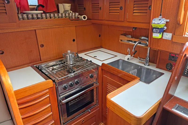 Raison D'etre Yacht Photos Pics 1988 Hallberg Rassy 42E yacht kitchen with stove, sink, and wooden cabinetry.