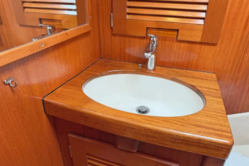 Raison D'etre Yacht Photos Pics Wooden bathroom sink in 1988 Hallberg Rassy 42E yacht, featuring elegant cabinetry and modern faucet.