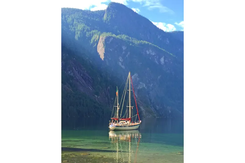 Raison D'etre Yacht Photos Pics Sailboat Hallberg Rassy 42E (1988) on tranquil water with scenic mountain backdrop.