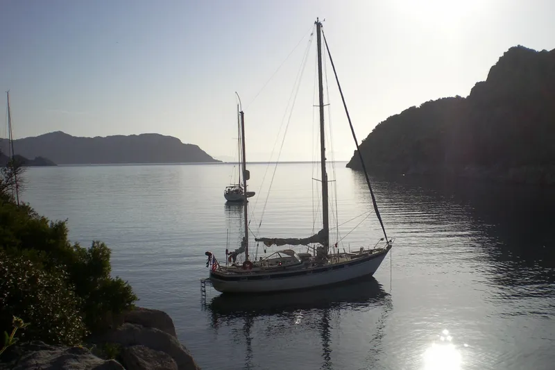 Raison D'etre Yacht Photos Pics Sailboat Hallberg Rassy 42E (1988) anchored in serene coastal waters at sunset.