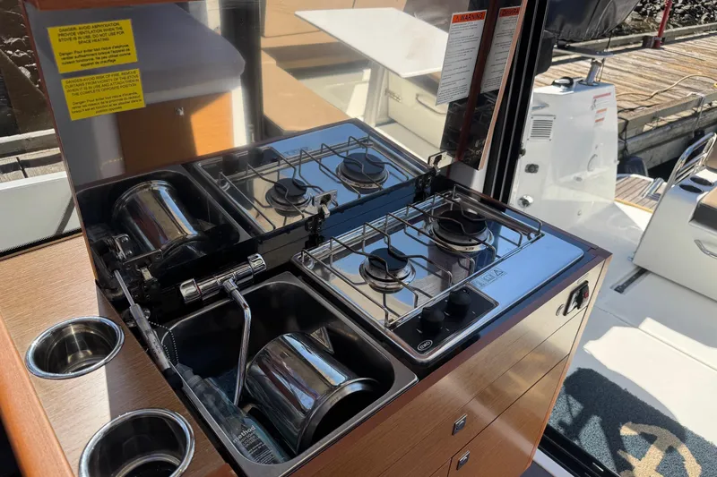  Yacht Photos Pics Compact kitchen area on 2017 Jeanneau 895 Offshore boat with dual-burner stove and sink.