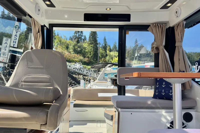  Yacht Photos Pics Interior of 2017 Jeanneau 895 Offshore boat with seating and table, docked near forested shoreline.