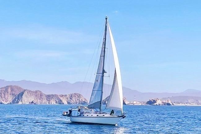 Sailboat Caliber 40LRC 2004 cruising on blue ocean with scenic rocky coastline.