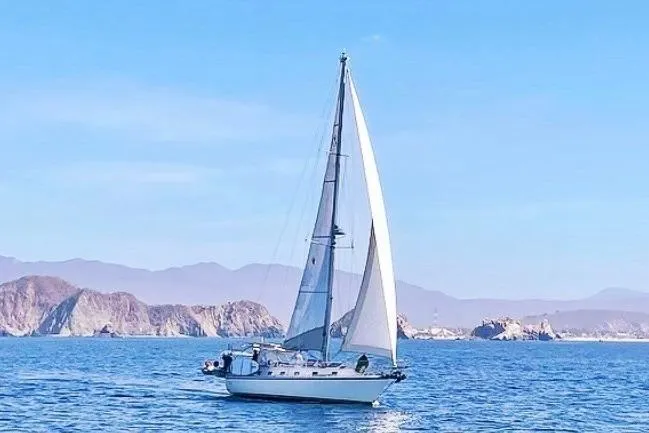Sailboat Caliber 40LRC 2004 cruising on blue ocean with scenic rocky coastline.