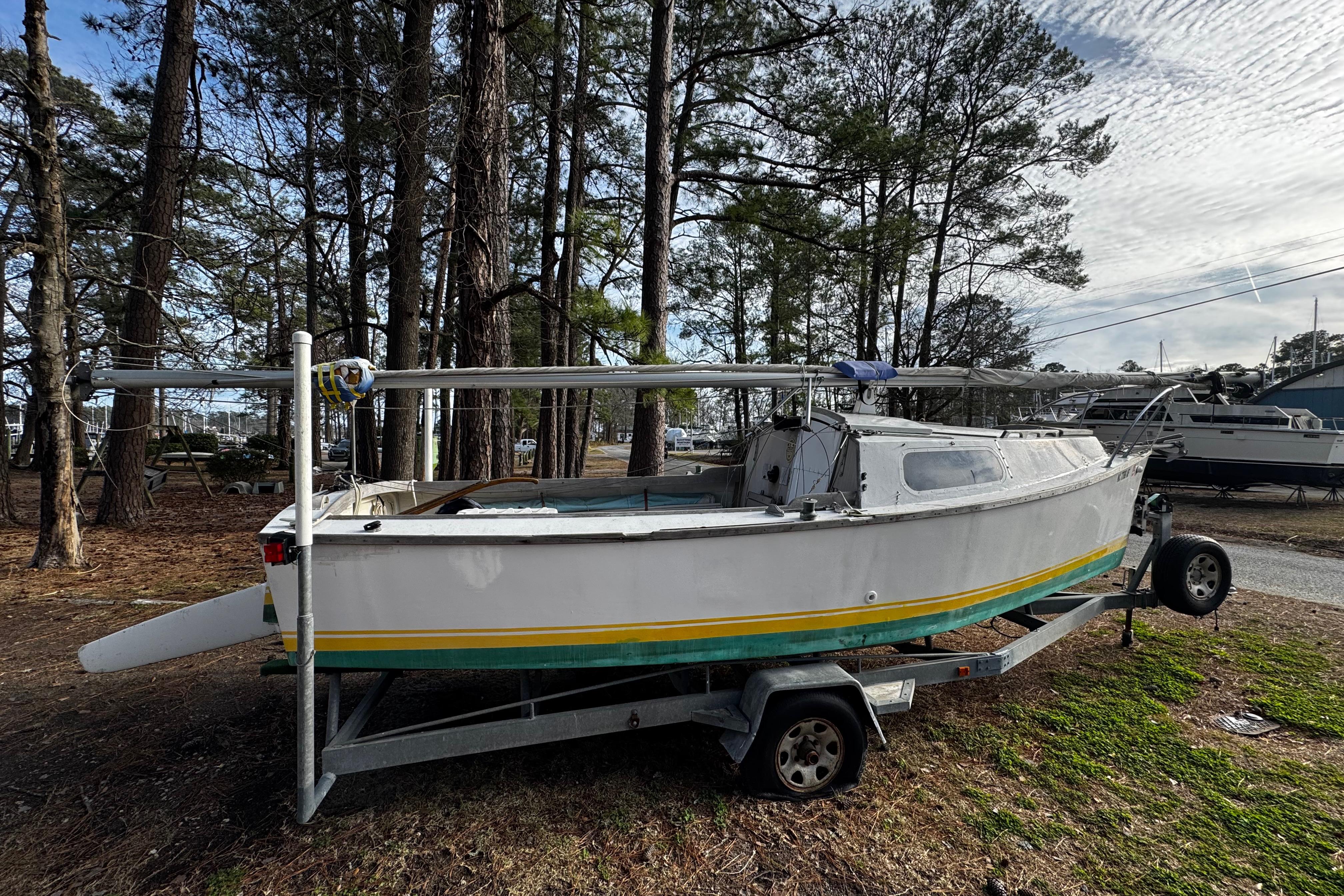 1976 Custom Wooden Sloop on trailer, surrounded by trees and parked outdoors.