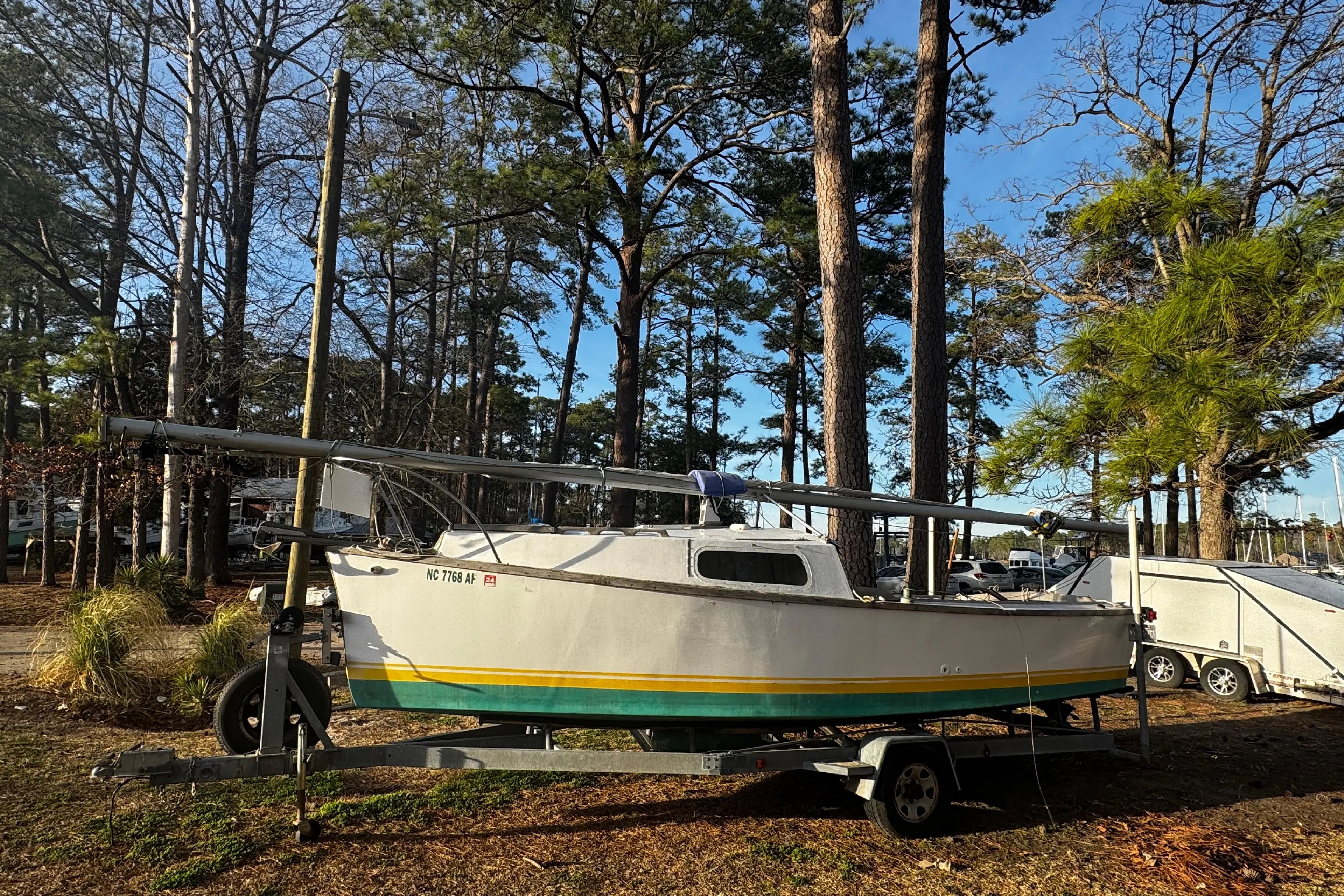 1976 Custom Wooden Sloop on trailer, surrounded by trees in a sunny setting.