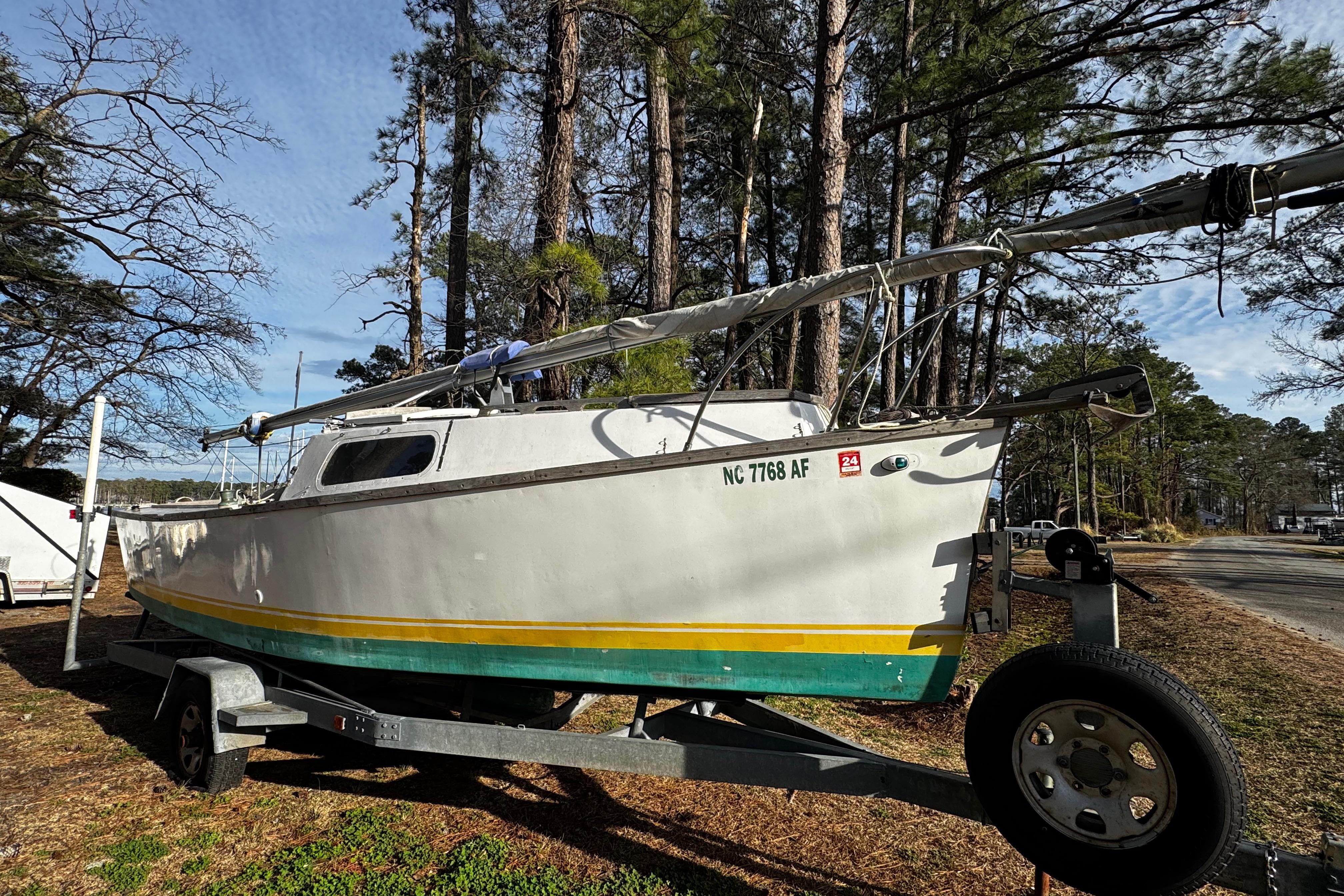 1976 Custom Wooden Sloop on trailer, surrounded by trees, under a clear sky.