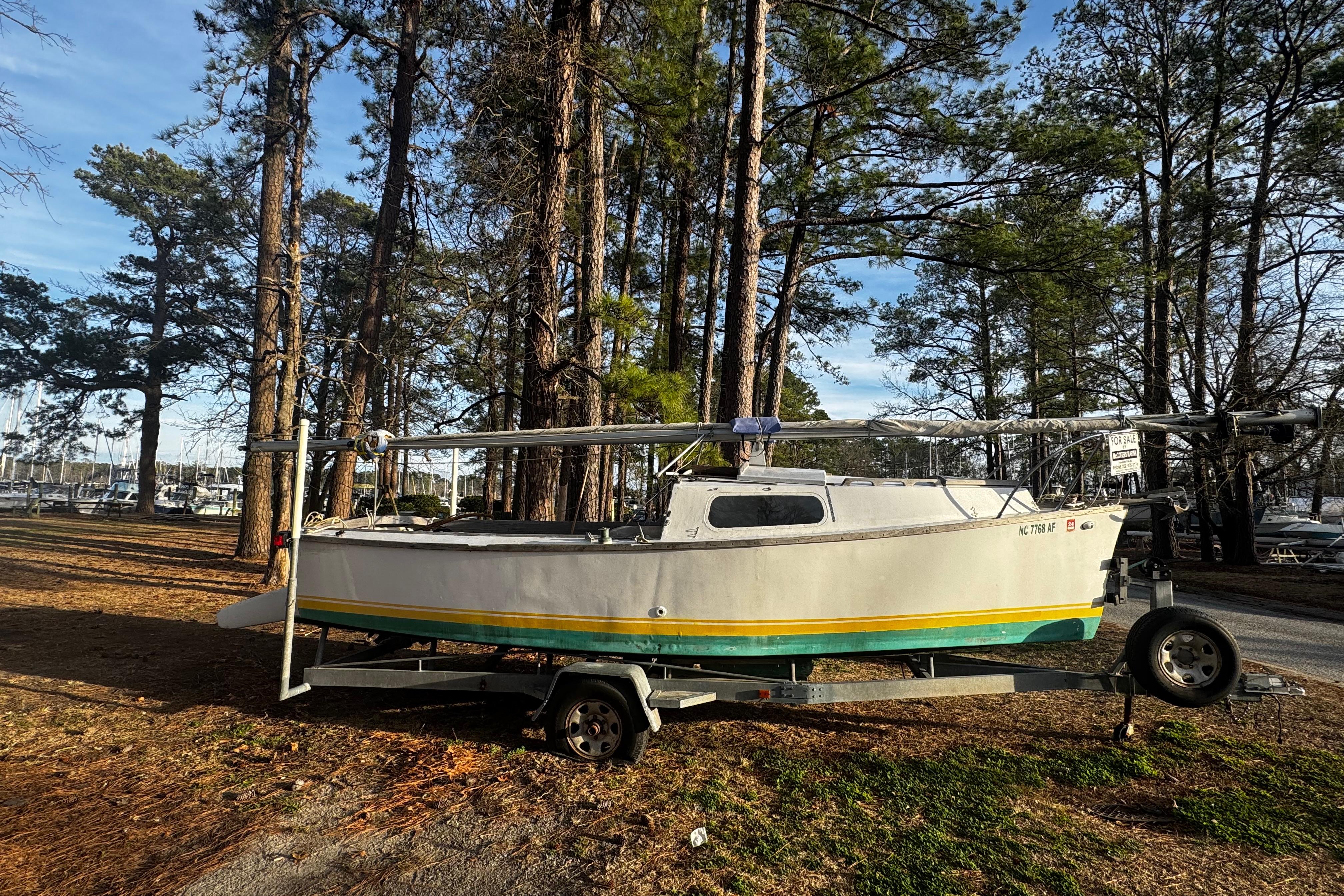 1976 Custom Wooden Sloop on trailer, surrounded by tall pine trees.
