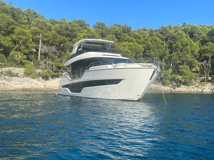  Yacht Photos Pics 2024 Cranchi 67 FLY yacht anchored near a forested shoreline.