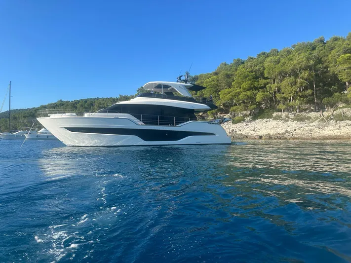  Yacht Photos Pics 2024 Cranchi 67 FLY yacht cruising near a forested coastline under a clear blue sky.
