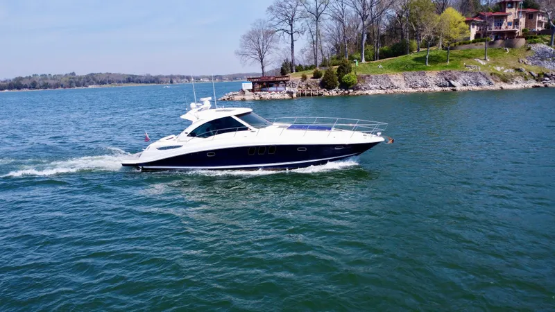  Yacht Photos Pics 2006 Sea Ray 48 Sundancer yacht cruising on a scenic lake near a wooded shoreline.