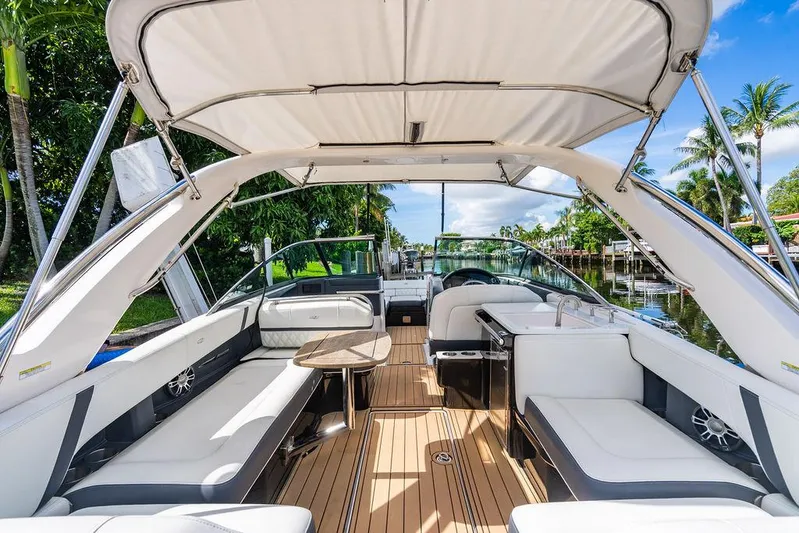 Dreamaker Yacht Photos Pics 2021 Regal 29 OBX boat interior with spacious seating and canopy, docked by lush greenery.