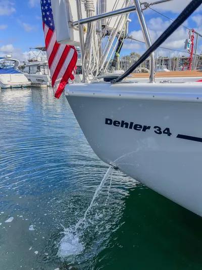 Anthem Yacht Photos Pics 2022 Dehler 34 sailboat with American flag in marina, water splashing from hull.