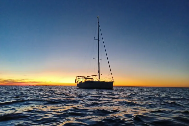 J'ouvert Yacht Photos Pics Sailboat Beneteau 43 (2009) silhouetted against a vibrant sunset over calm ocean waters.