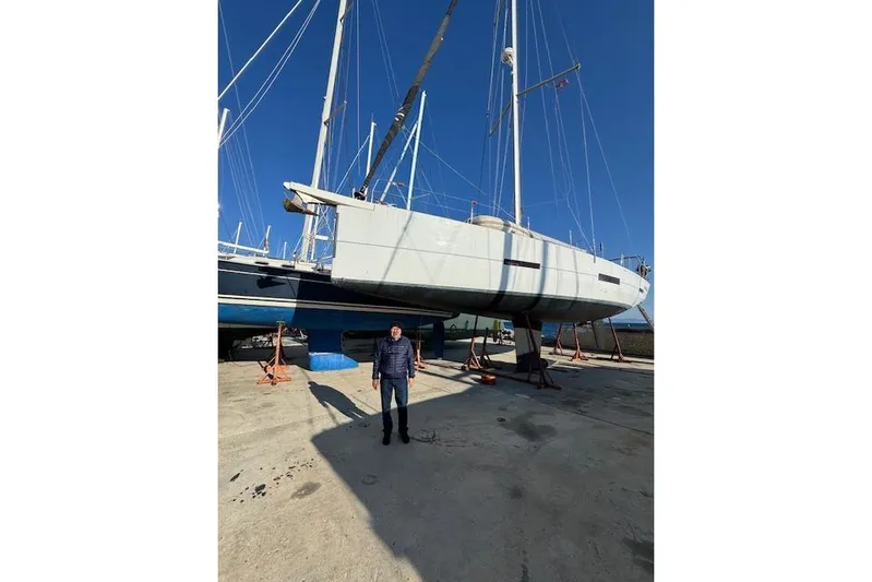  Yacht Photos Pics Man standing beside a 2015 Dufour 560 Grand Large sailboat on dry dock.