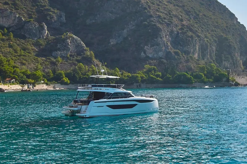  Yacht Photos Pics Prestige M48 2025 yacht cruising in clear blue waters near a rocky coastline.