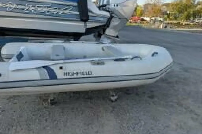 Dolce Vita Yacht Photos Pics White inflatable Highfield boat on a trailer, parked outdoors near a larger vessel.