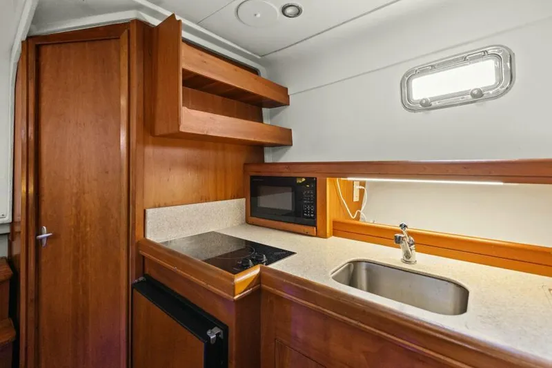 Whattakeeper Yacht Photos Pics 2006 Mainship 34 Rum Runner II galley with sink, stove, microwave, and wooden cabinetry.